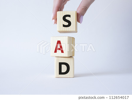 Sad symbol. Wooden cubes with words Sad. Businessman hand. Beautiful white background. Business and Sad concept. Copy space. Sad symbol. Wooden cubes with words Sad. Businessman hand. Beautiful white background. Business and Sad concept. Copy space. 112654017