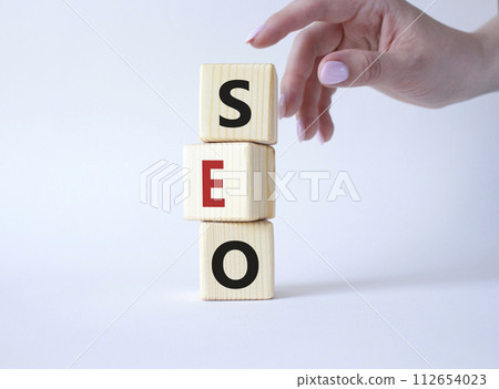 SEO - Search Engine Optimization symbol. Wooden blocks with words SEO. Businessman hand. Beautiful white background. Business and SEO concept. Copy space. 112654023