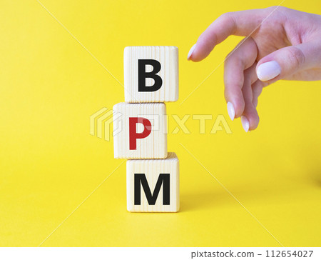 BPM - Business Process Management symbol. Wooden cubes with words BPM. Businessman hand. Beautiful yellow background. Business and BPM concept. Copy space. 112654027