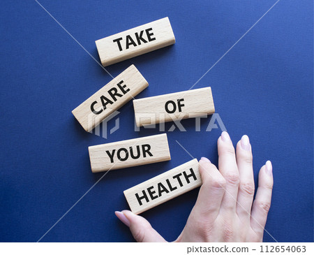 Health symbol. Wooden blocks with words Take Care of your Health. Doctor hand. Beautiful deep blue background. Health concept. Copy space. 112654063
