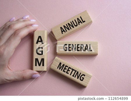 AGM - Annual general meeting symbol. Concept word AGM on wooden blocks. Businessman hand. Beautiful pink background. Business and AGM concept. Copy space. 112654899