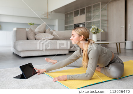 Young woman practices yoga at home, with tablet pc next to her, classes at home 112656470