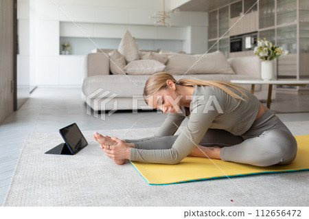 Young woman practices yoga at home, with tablet pc next to her, classes at home 112656472