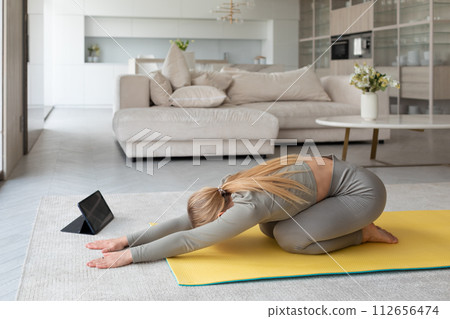 Young woman practices yoga at home, with tablet pc next to her, classes at home Young woman practices yoga at home, with tablet pc next to her, classes at home 112656474