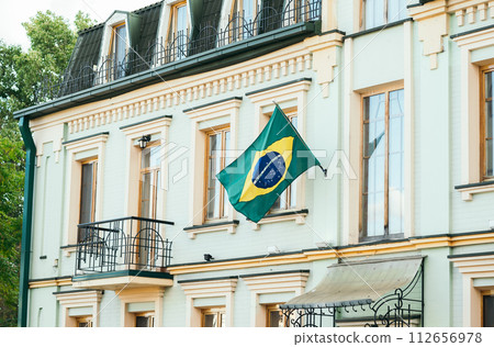 The green Flag of the country of Brazil flutters in the wind against the yellow wall of the house. The green Flag of the country of Brazil flutters in the wind against the yellow wall of the house. 112656978