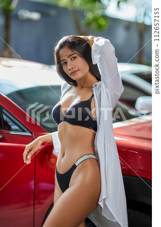 A young beautiful girl in a white shirt and black lingerie posing in the parking area 112657155
