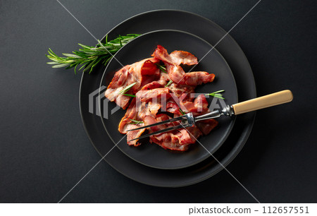 Roasted bacon slices with rosemary on a black plate. 112657551