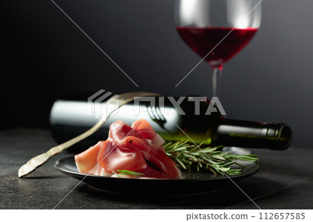 Prosciutto with rosemary and red wine on a black background. 112657585