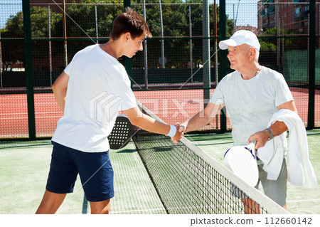 Senior and young man shake hands before padel tennis match 112660142