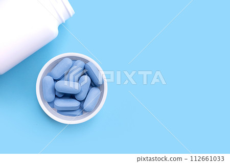 PrEP ( Pre-Exposure Prophylaxis) used to prevent HIV, in plastic pill bottle cap on blue background, Copy space 112661033