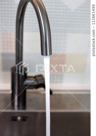 Water flowing out of a stainless steel tap. Kitchen room Water flowing out of a stainless steel tap. Kitchen room 112661499