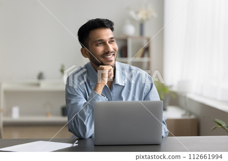 Pensive satisfied Indian man sitting at desk with laptop Pensive satisfied Indian man sitting at desk with laptop 112661994