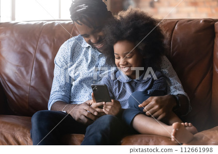 African dad and cute little daughter play game on cellphone African dad and cute little daughter play game on cellphone 112661998