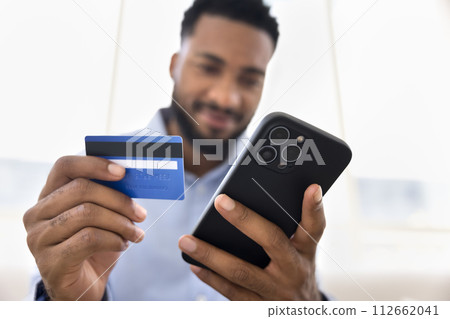 Positive young African man holding blue plastic credit card Positive young African man holding blue plastic credit card 112662041