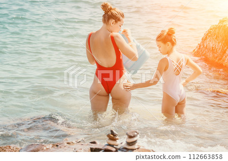 Woman and her daughter practicing balancing yoga pose on one leg up together on rock in the sea. Silhouette mother and daughter doing yoga at beach 112663858