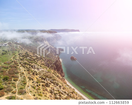 Aerial view. The drone flies over foggy and fluffy clouds. Blue sky sun and sea fog. Abstract aerial nature summer ocean sunset sea and sky background. Horizon. Vacation, travel and holiday concept 112663859