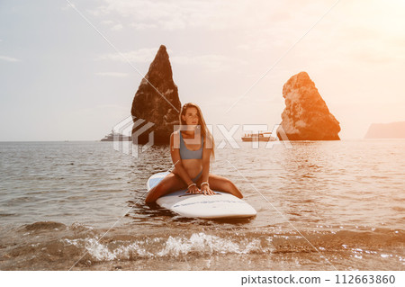 Woman sea sup. Close up portrait of happy young caucasian woman with long hair looking at camera and smiling. Cute woman portrait in bikini posing on sup board in the sea Woman sea sup. Close up portrait of happy young caucasian woman with long hair looking at camera and smiling. Cute woman portrait in bikini posing on sup board in the sea 112663860