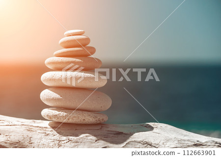 Pyramid stones on the seashore on a sunny day on the blue sea background. Happy holidays. Pebble beach, calm sea, travel destination. Concept of happy vacation on the sea, meditation, spa, calmness. 112663901