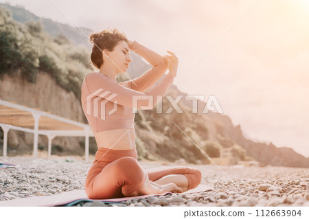 Middle aged well looking woman with black hair, fitness instructor in leggings and tops doing stretching and pilates on yoga mat near the sea. Female fitness yoga routine concept. Healthy lifestyle 112663904