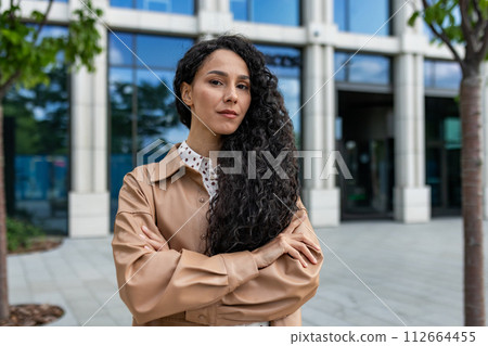 A professional woman stands confidently outside a modern office building, arms crossed with a powerful stance. A professional woman stands confidently outside a modern office building, arms crossed with a powerful stance. 112664455