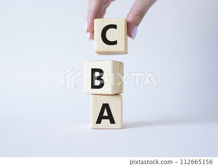 CBA - Cost Benefit Analysis symbol. Wooden cubes with word CBA. Beautiful white background. Businessman hand. Business and Cost Benefit Analysis concept. Copy space. CBA - Cost Benefit Analysis symbol. Wooden cubes with word CBA. Beautiful white background. Businessman hand. Business and Cost Benefit Analysis concept. Copy space. 112665156