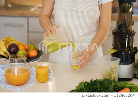 Middle selection of woman pouring fresh juice into glass. Homemade vegan beverage. Green drink 112665204