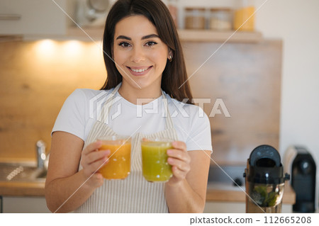 Portrait of beautiful woman holding two glasses of different beverage in hands. Healthy vegan drink Portrait of beautiful woman holding two glasses of different beverage in hands. Healthy vegan drink 112665208