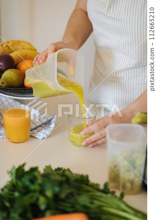 Middle selection of woman pouring fresh juice into glass. Homemade vegan beverage. Green drink Middle selection of woman pouring fresh juice into glass. Homemade vegan beverage. Green drink 112665210