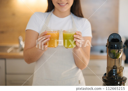 Middle selection of woman hold two different glasses of homemade juice. Orange and green colour beverage 112665215
