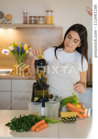 Young woman put celery into juicer. Process of making healthy drink. Young woman put celery into juicer. Process of making healthy drink. 112665286
