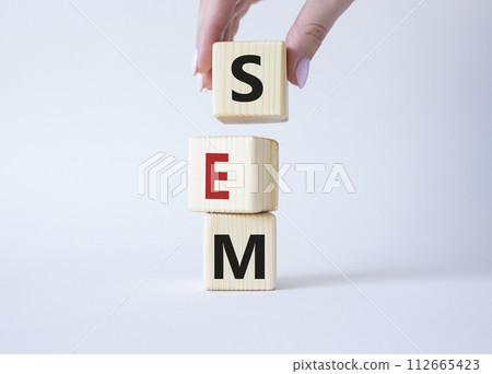 SEM - Search Engine Marketing symbol. Wooden cubes with words SEM. Businessman hand. Beautiful white background. Business and SEM concept. Copy space. 112665423