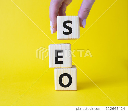 SEO - Search Engine Optimization symbol. Wooden blocks with words SEO. Businessman hand. Beautiful yellow background. Business and SEO concept. Copy space. 112665424