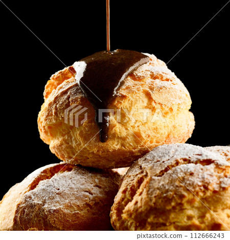 Sprinkle chocolate sauce on a small pile of custard cream puffs 112666243