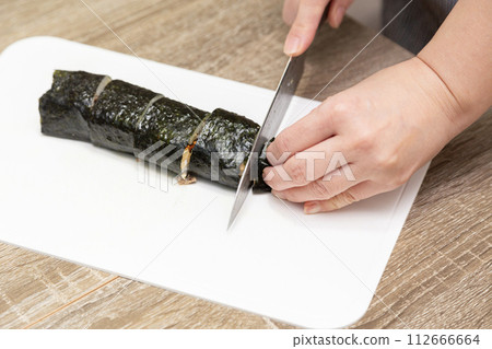 Woman's hands cutting sushi rolls 112666664