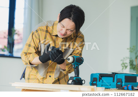 一個年輕人用電動螺絲起子工作 112667182
