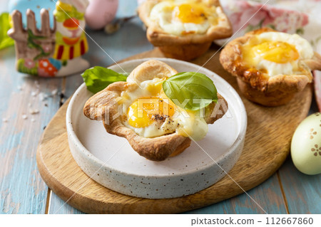 Scrambled eggs in puff pastry with cheese and bacon. Easter breakfast on a festive table. Scrambled eggs in puff pastry with cheese and bacon. Easter breakfast on a festive table. 112667860
