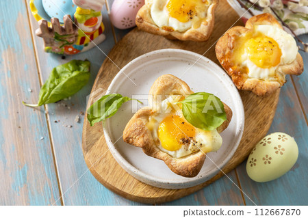 Scrambled eggs in puff pastry with cheese and bacon. Easter breakfast on a festive table. View from above. Scrambled eggs in puff pastry with cheese and bacon. Easter breakfast on a festive table. View from above. 112667870
