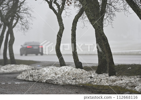 melting snow on the lawn and a car on the road in the fog in a small town in Finland 112668116