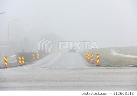 foggy road with roadwork signs and car 112668118