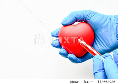 The doctor's hand was wearing a blue glove, holding a heart and a red syringe. Concept of Coronary Angiography (CAG). Close-up, copy space on left for design or text, blurred white background 112668986