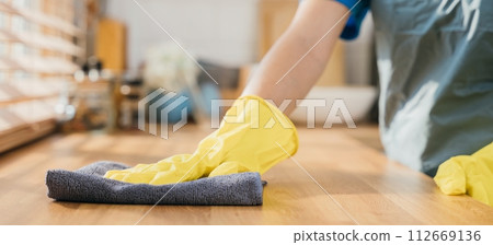 Maid in protective glove cleans wood table in cozy kitchen. Using professional cleaning products for perfect home tidiness. Cleaner working safety glove hygiene routine. Maid housekeeping concept. 112669136