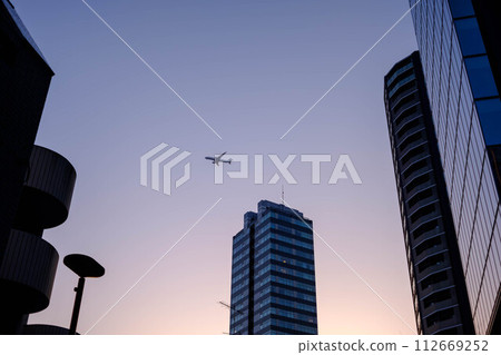Airplane flying between buildings at dusk 112669252