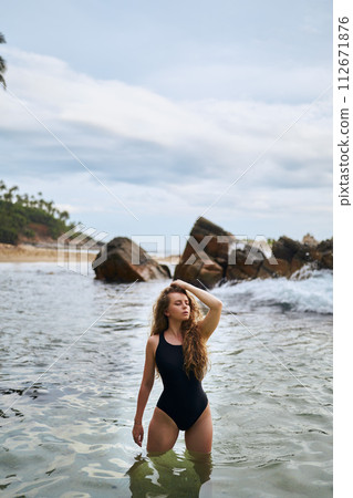 Attractive woman in swimsuit enjoys sea dip by rocks. Tranquil ocean scene with female model. Wellness, swimwear fashion, serene holiday. Solo traveler explores coastal beauty, healthy living. Attractive woman in swimsuit enjoys sea dip by rocks. Tranquil ocean scene with female model. Wellness, swimwear fashion, serene holiday. Solo traveler explores coastal beauty, healthy living. 112671876