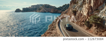 Drone view of a car driving on a road that cuts through mountains and sea. 112673084