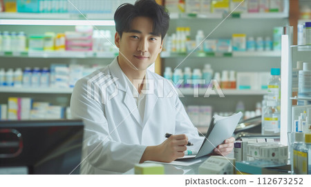 Asian male pharmacist checking documents in pharmacy. 112673252