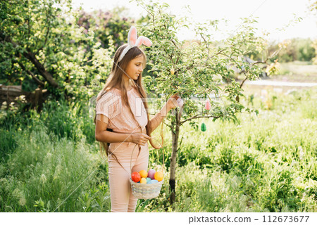 Cute funny girl with Easter eggs and bunny ears at garden. easter concept. Laughing child at Easter egg hunt. Child in park with basket full of eggs, spring concept Cute funny girl with Easter eggs and bunny ears at garden. easter concept. Laughing child at Easter egg hunt. Child in park with basket full of eggs, spring concept 112673677
