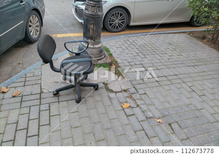 A black office chair stands on a city sidewalk. Strange things on the streets of cities, it's not clear why they are here A black office chair stands on a city sidewalk. Strange things on the streets of cities, it's not clear why they are here 112673778