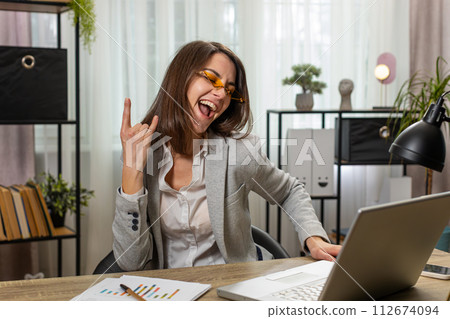 Happy business woman working on laptop at home office desk putting on earbuds listening music relax 112674094