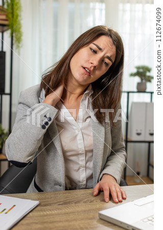 businesswoman suffers from spine neck muscle pain at home office working on laptop overworking 112674099