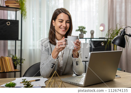 Businesswoman drinking cup of warm hot coffee sitting at table office workplace relax taking a break 112674135